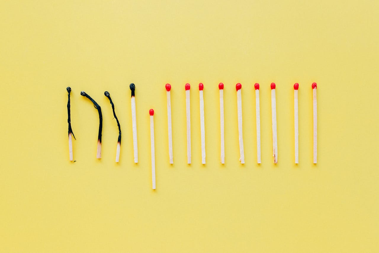 Artistic flat lay of burnt and unlit matches on a yellow surface, symbolizing burnout.